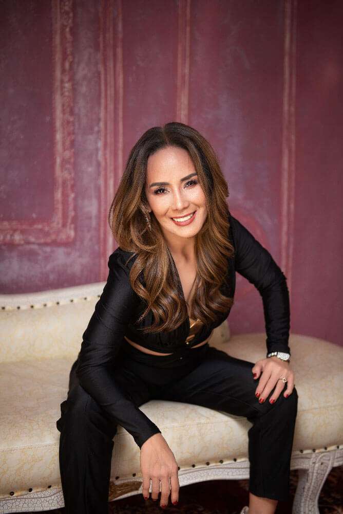 Imee sitting on a vintage couch in a black outfit during her 60th birthday portrait session in Brisbane