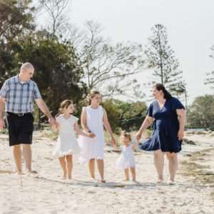 Family of four walking hand-in-hand along a sandy path at Wynnum Manly, family photography by Twin Lotus Production, Brisbane family photographer