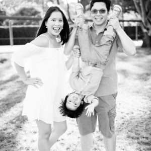 Mum laughing while dad playfully swings their child upside down, black-and-white family portrait by Twin Lotus Production, Brisbane family photographer