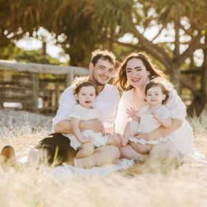 Parents sitting with their two young children in a sunlit Brisbane field, family photography by Twin Lotus Production, Brisbane family photographer