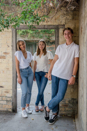 Three siblings in casual white and denim outfits in an urban laneway, family portrait by Twin Lotus Production, Brisbane family photographer