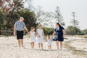 Family of four walking hand-in-hand along a sandy path at Wynnum Manly, family photography by Twin Lotus Production, Brisbane family photographer
