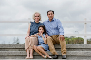 Parents smiling with their daughter in coordinated blue outfits during a Brisbane family portrait session by Twin Lotus Production, Brisbane family photographer
