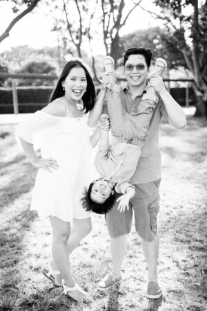 Mum laughing while dad playfully swings their child upside down, black-and-white family portrait by Twin Lotus Production, Brisbane family photographer