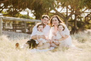 Parents sitting with their two young children in a sunlit Brisbane field, family photography by Twin Lotus Production, Brisbane family photographer